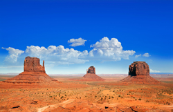 Southwestern landscape with three mesas in the distance under a clear blue sky.